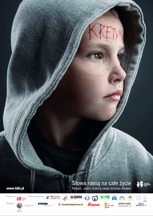 Plakat z chłopcem około 4 lat w kapturze z krwawym napisem na czole Kretyn. Hasło Słowa ranią na całe życie